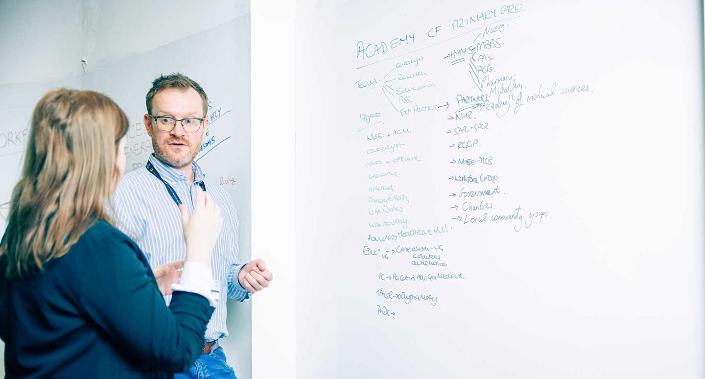 Two members of the Academy of Primary Care in a discussion by a whiteboard