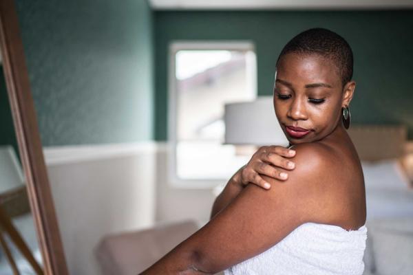 Woman wearing a towel applying moisturiser