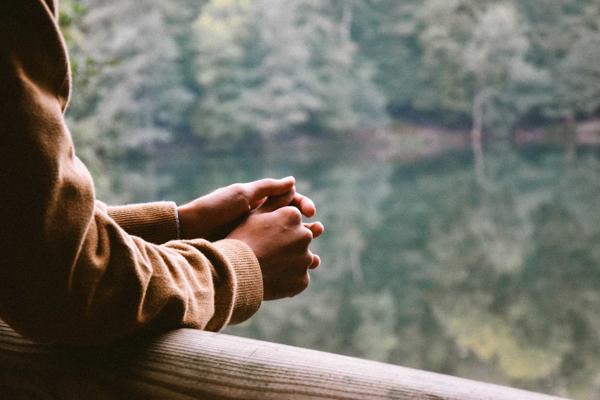 Person leaning on a handrail with only hands and arms in view, hands clasped